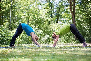 Zwei Personen üben Yoga im Grünen.